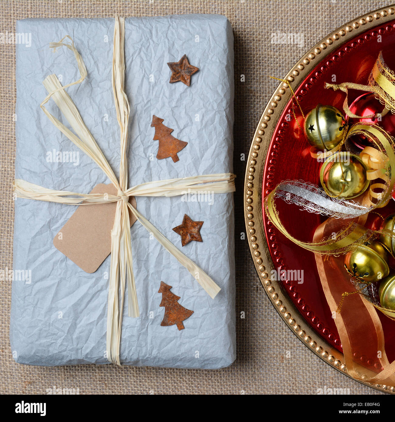 High angle closeup of a tissue wrapped Christams Present and ornaments on a burlap surface. Square Format. Stock Photo