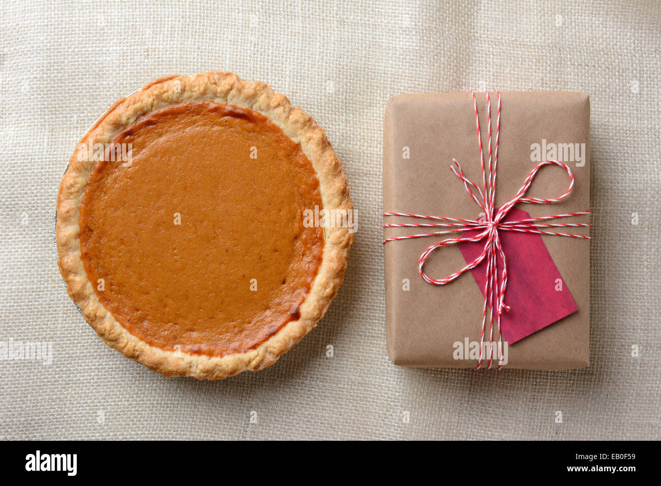 High angle shot of a holiday pumpkin pie and plain paper wrapped present. The brown gift is tied with red and white string Stock Photo