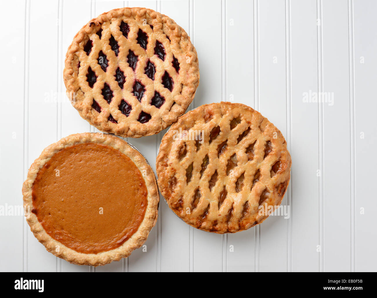 High angle shot of three pies, apple, pumpkin, and cherry. Horizontal format on a white beadboard surface. Stock Photo