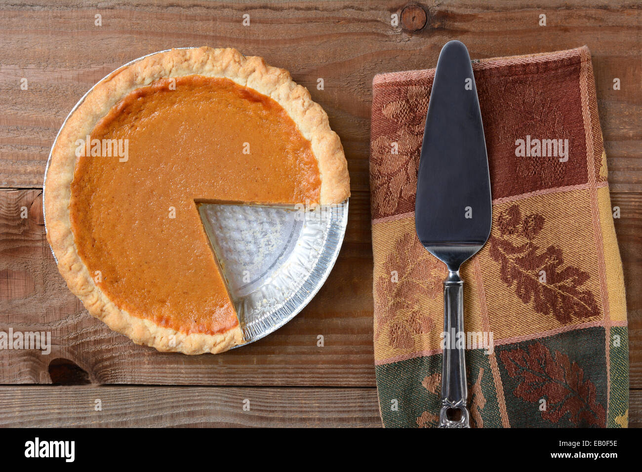 High angle shot of a pumpkin pie that has been cut into. Shot on a rustic wood table with a Autumn themed napkin and server by i Stock Photo