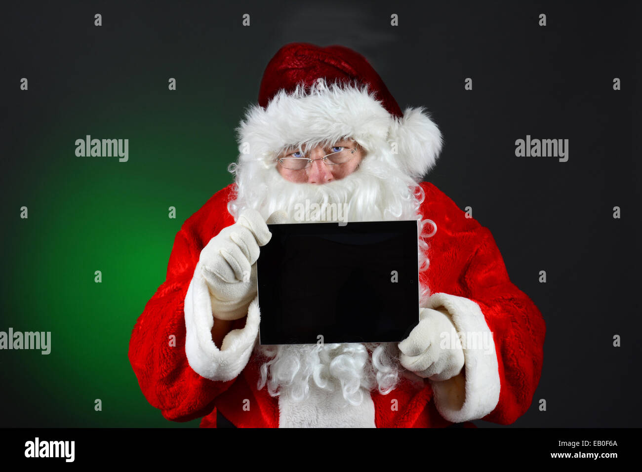 Santa Claus holding a tablet computer with its blank screen facing the viewer. Horizontal format on a light to dark green Stock Photo