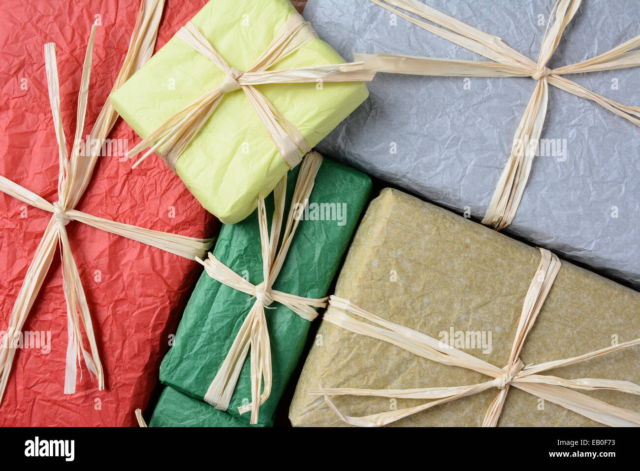 High angle closeup shot of a group of Christmas presents wrapped with colorful tissue paper. The gifts are tied with raffia. Stock Photo