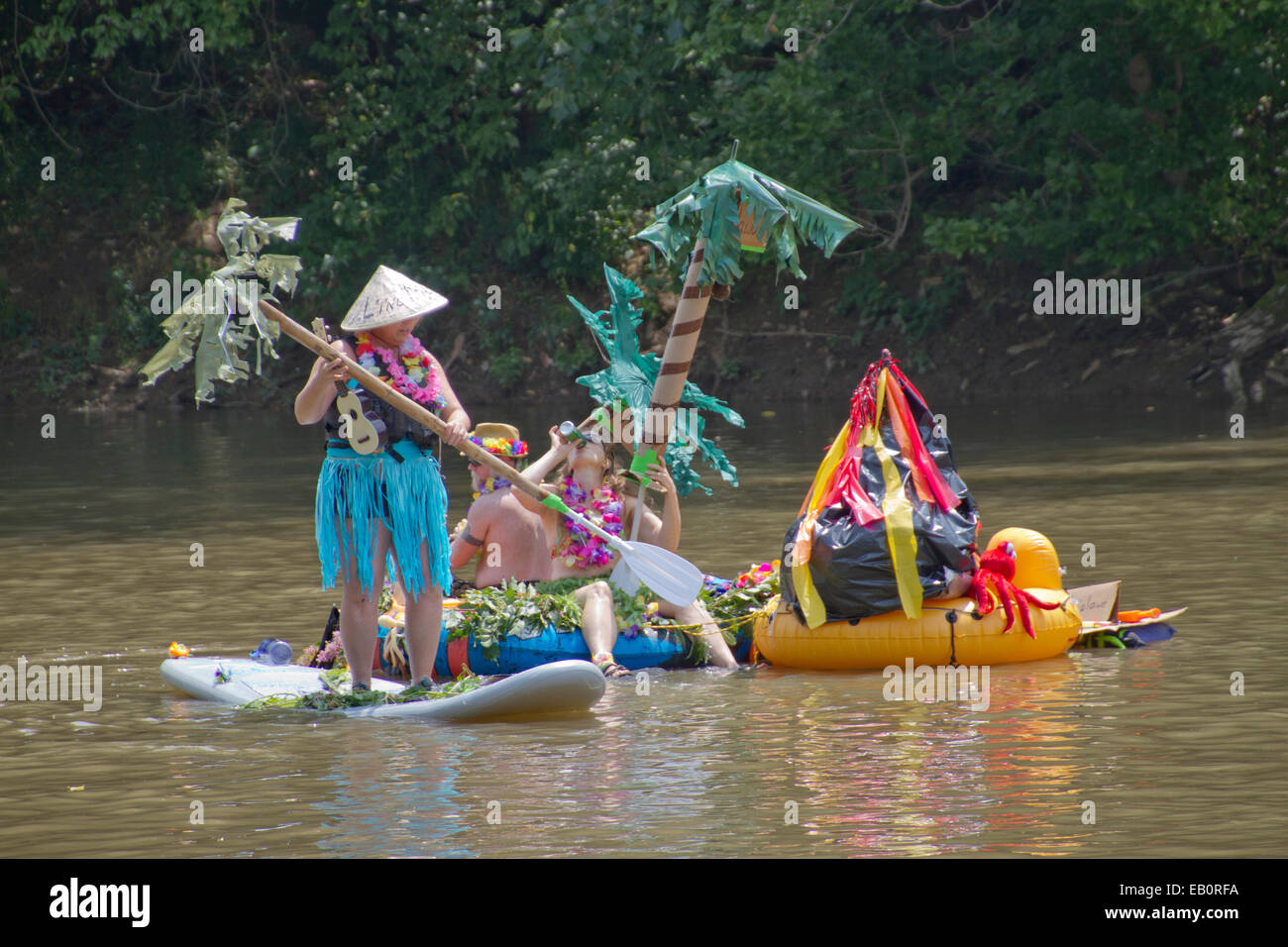Costumed people float down the French Broad River on a creative palm island surfboard in the