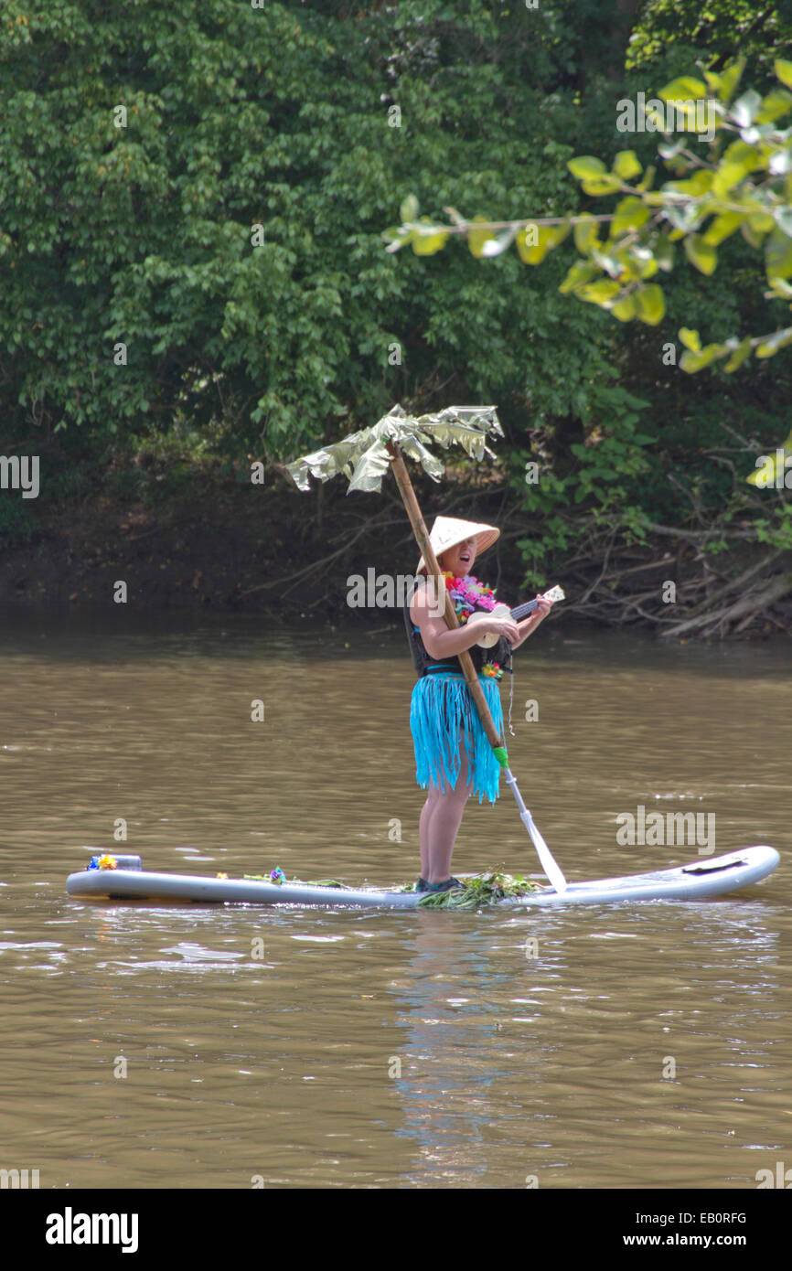 Woman sings and plays a ukulele floating down a river on a surfboard with a palm tree in the