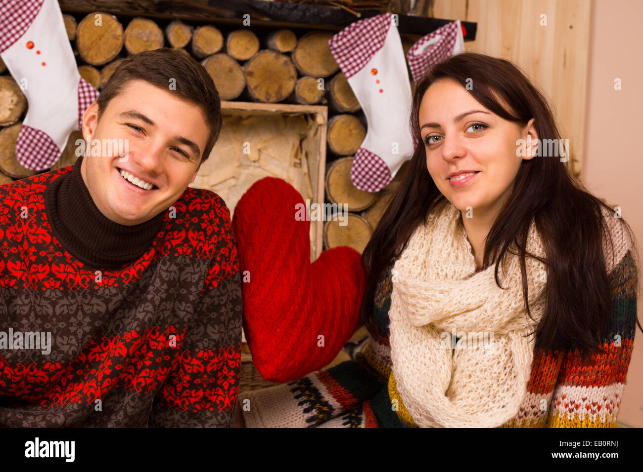 Romantic young couple celebrating Christmas in a rustic wooden cabin decorated with traditional Xmas stockings and a big red heart. Stock Photo