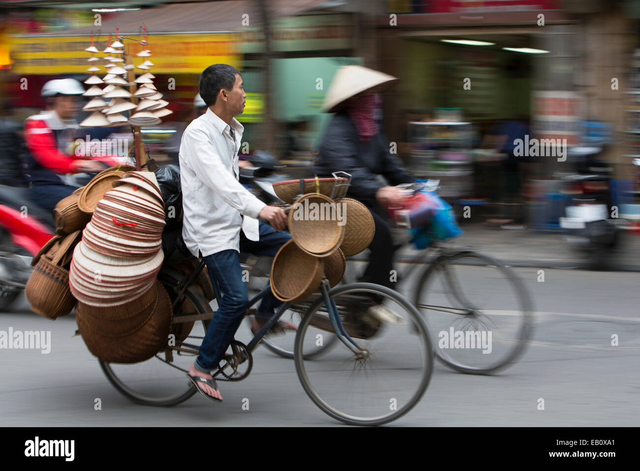 Vendor riding bicycle carrying NonLa hats for sale in Hanoi Vietnam Stock Photo