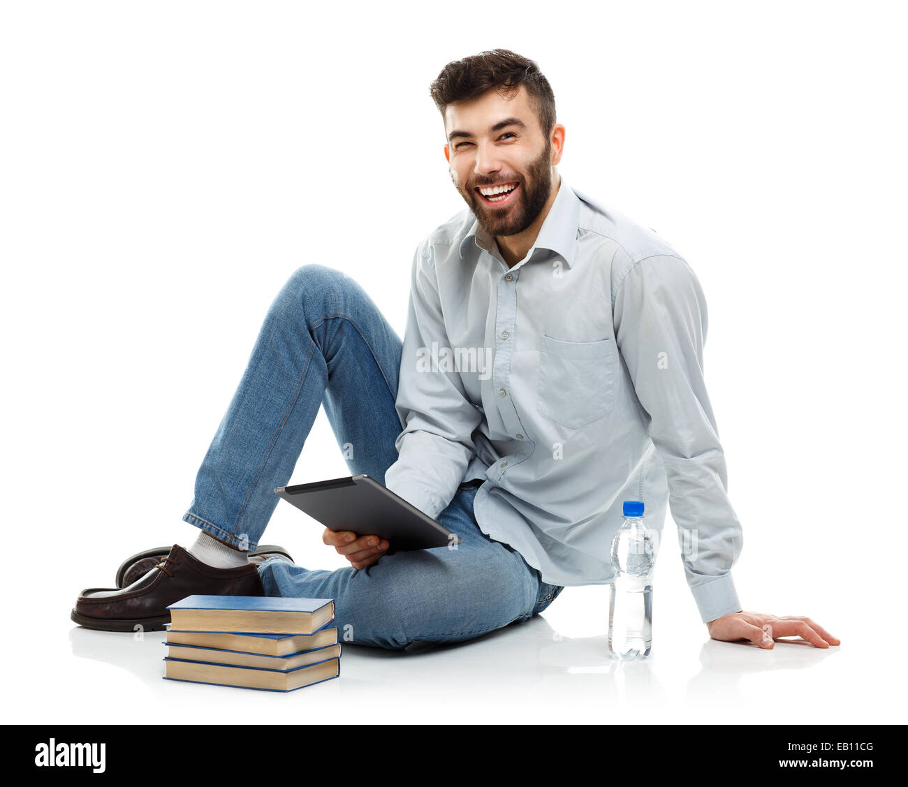 Young bearded smiling man holding a tablet with books and a bottle of water sitting on a white background Stock Photo