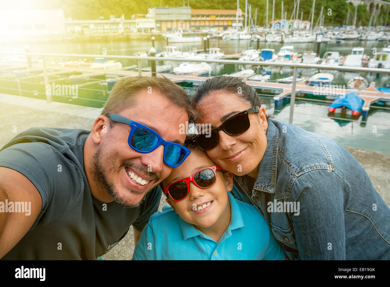 Family having fun wearing sunglasses & waving to a camera taking selfie photograph on summer holiday Stock Photo