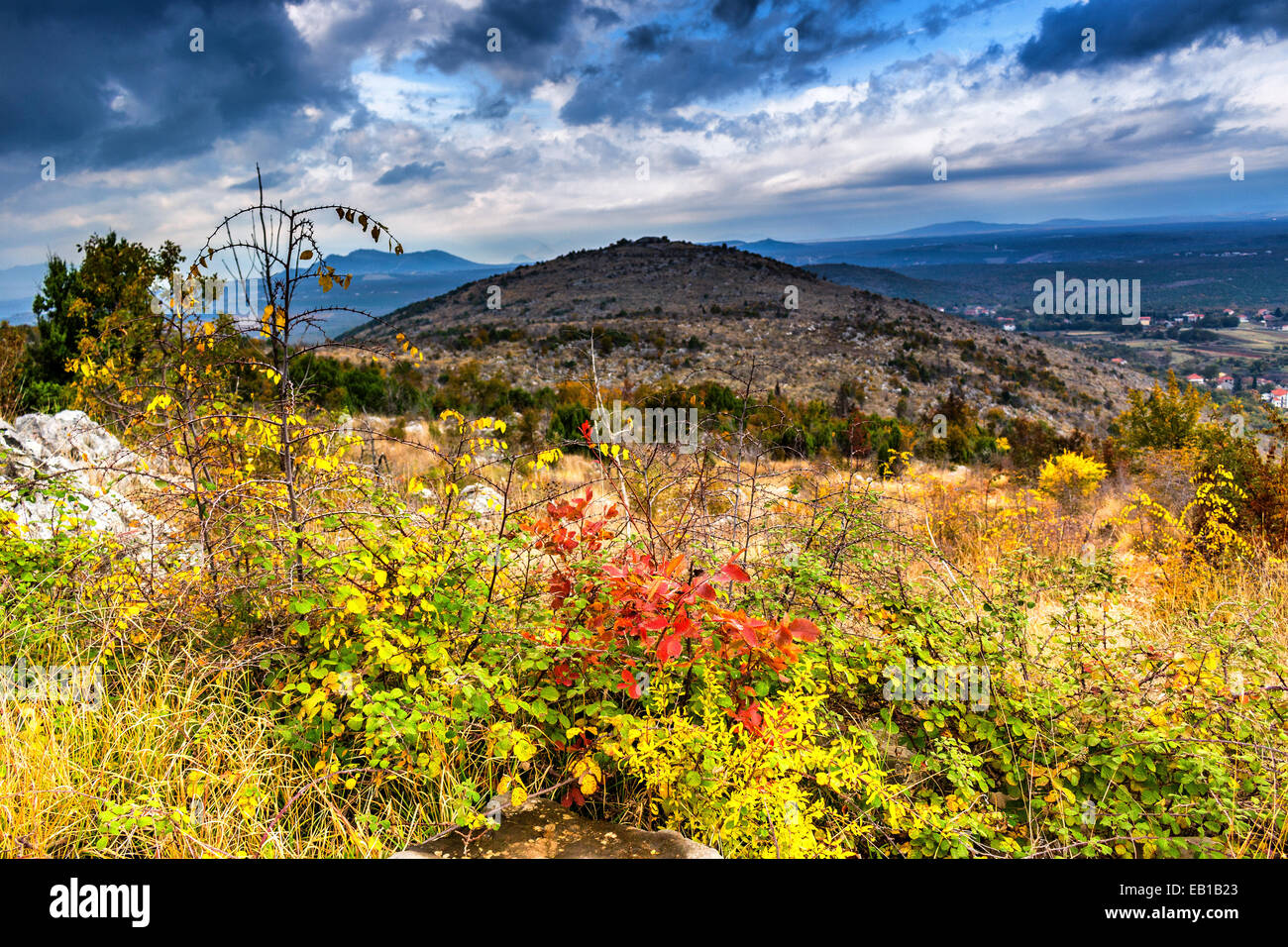 Autumn View of the Krizevac (Cross) Mountain in Medjugorje in Bosnia ed Erzegovina: brownish trees, green weeds, orange and yellow leaves and grey rocks Stock Photo