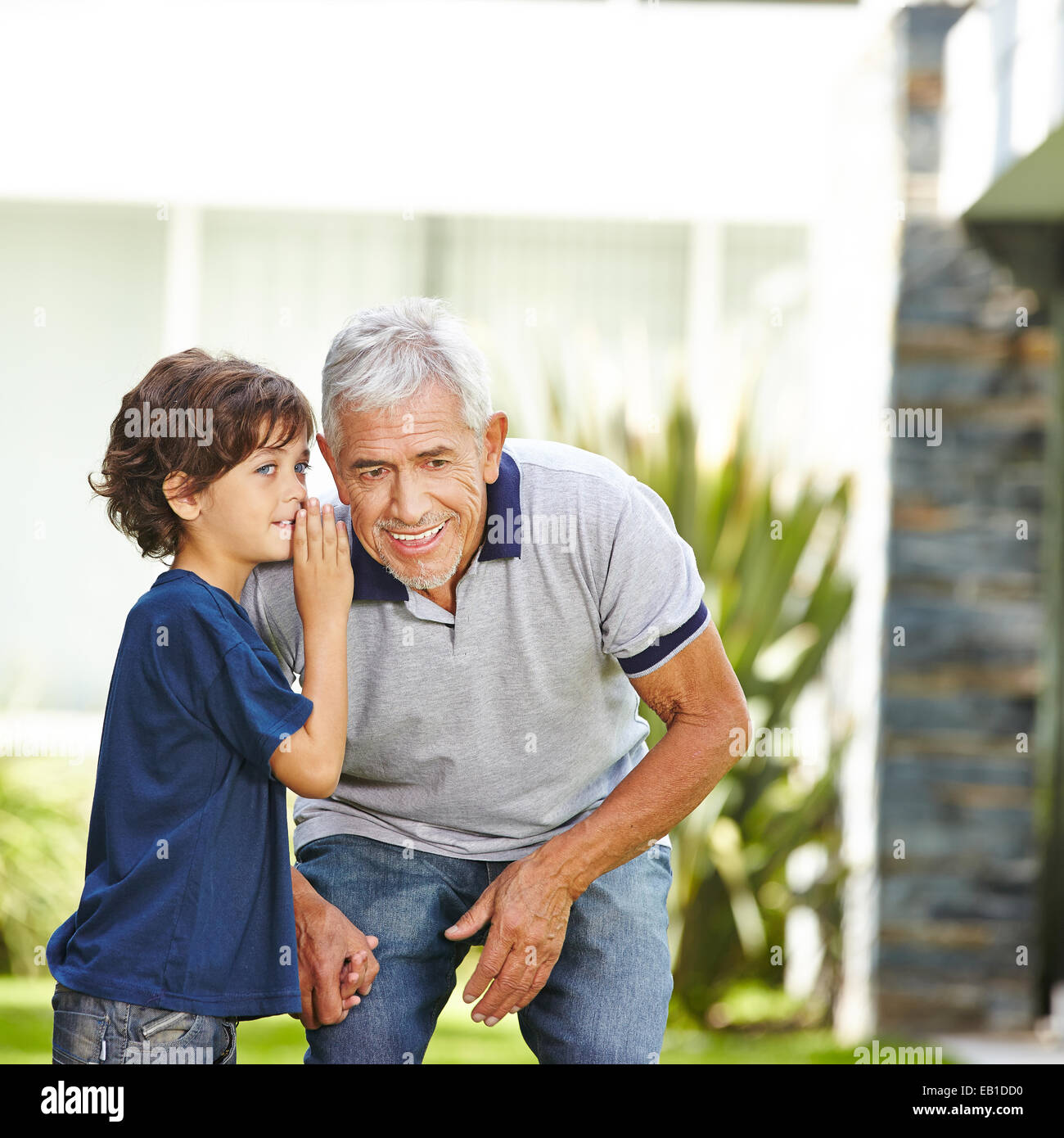 Grandson whispering a secret in the ear of his grandfather outdoors Stock Photo