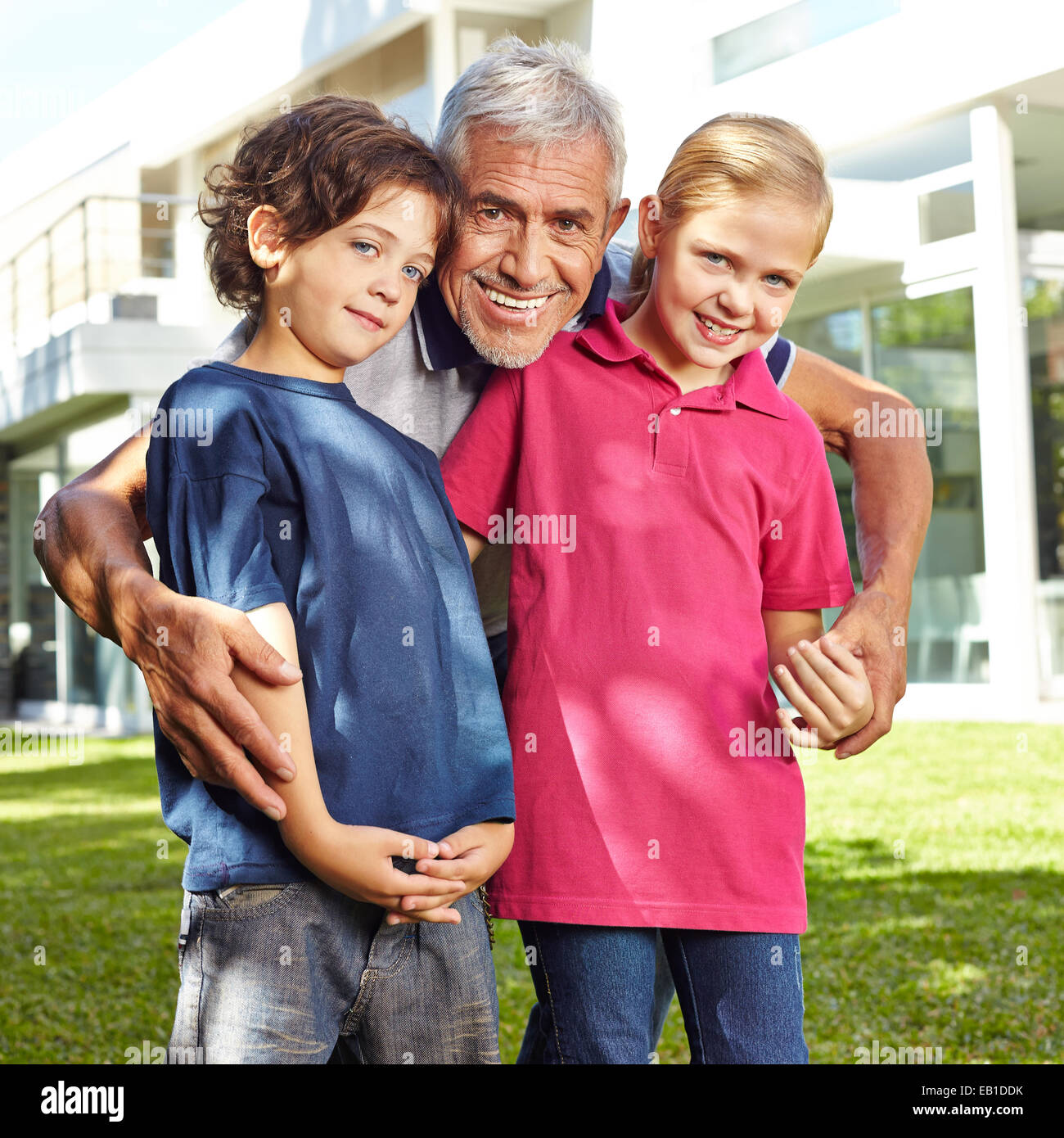 Happy grandfather with two grandchildren in a garden in front of a house Stock Photo