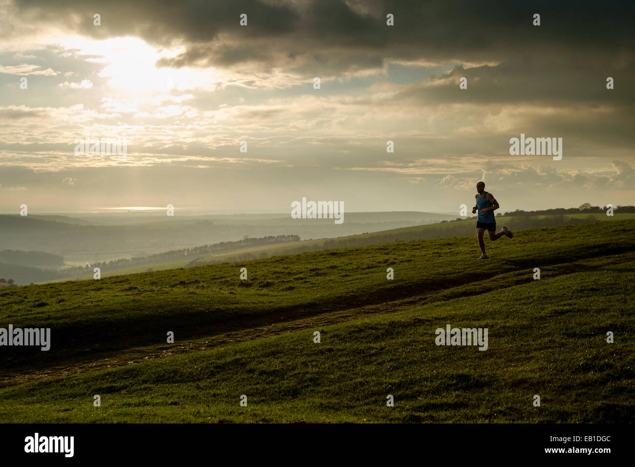 A runner exercises on the South Downs at Chanctonbury Ring as the sun sets. Picture by Julie Edwards Stock Photo