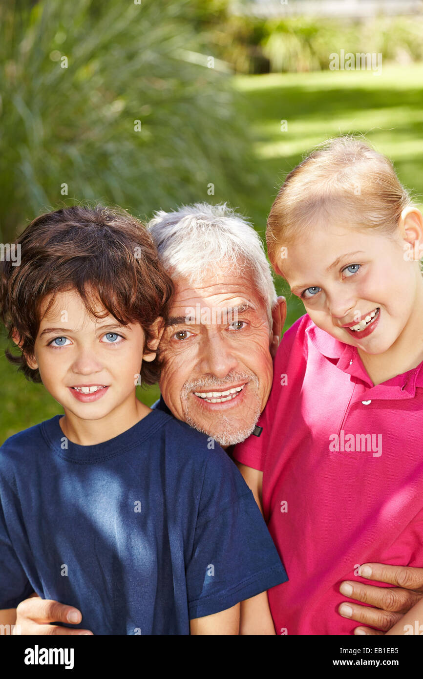 Grandfather laughing outside with two grandchildren in a garden Stock Photo