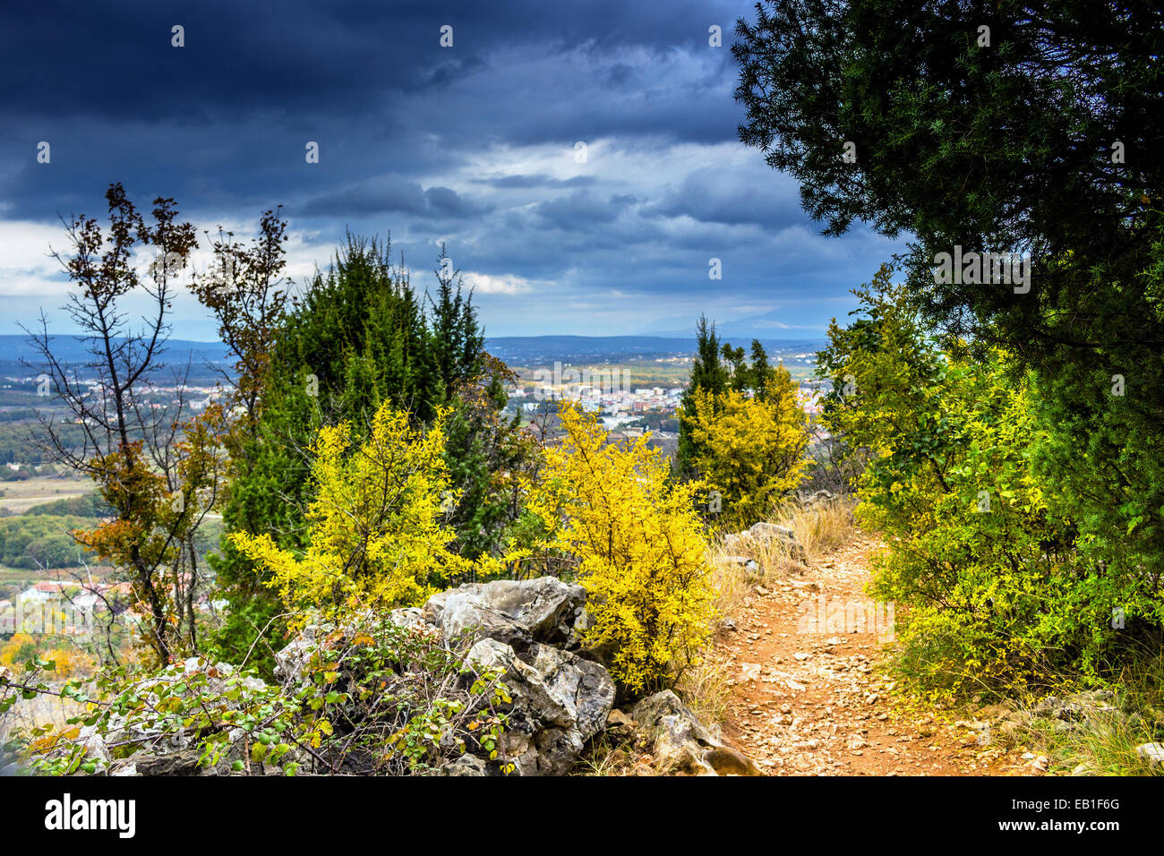 Autumn View of the Krizevac (Cross) Mountain in Medjugorje in Bosnia ed Erzegovina: brownish trees, green weeds, orange and yellow leaves and grey rocks Stock Photo