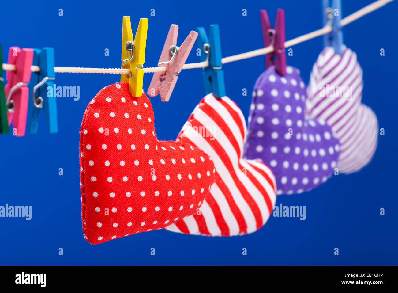 hearts hanging on a clothesline with clothespins, focus on red. Blue background Stock Photo