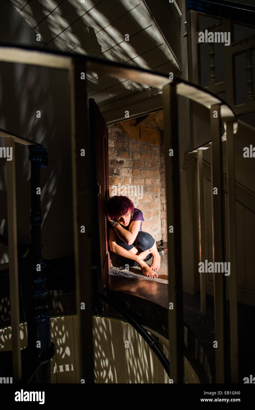 A young scared afraid worried teenage girl woman cowering in a secret room cupboard hiding place Stock Photo