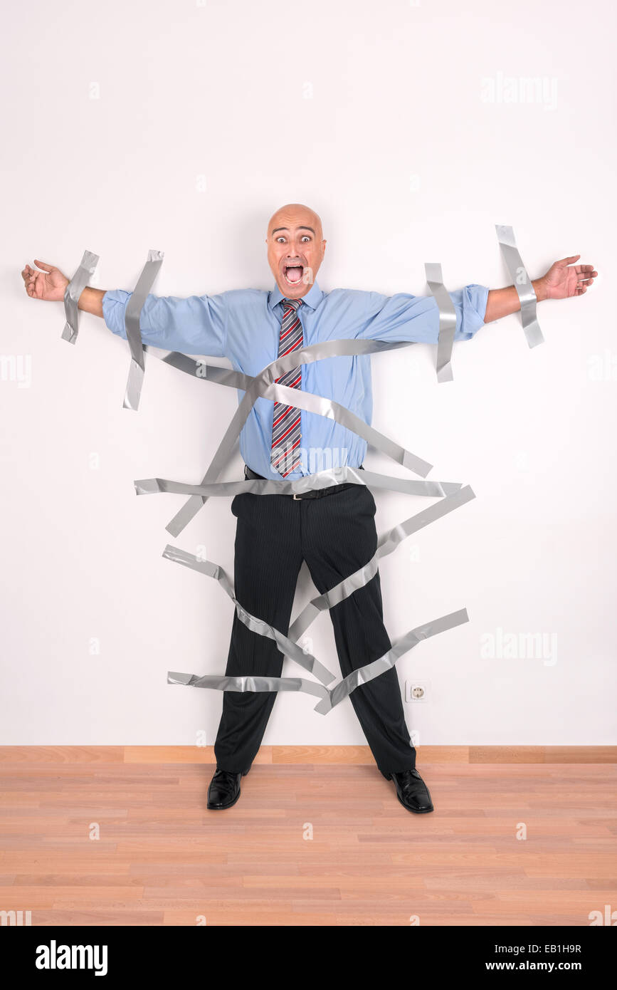 Businessman screaming, glued to the wall with duct tape Stock Photo