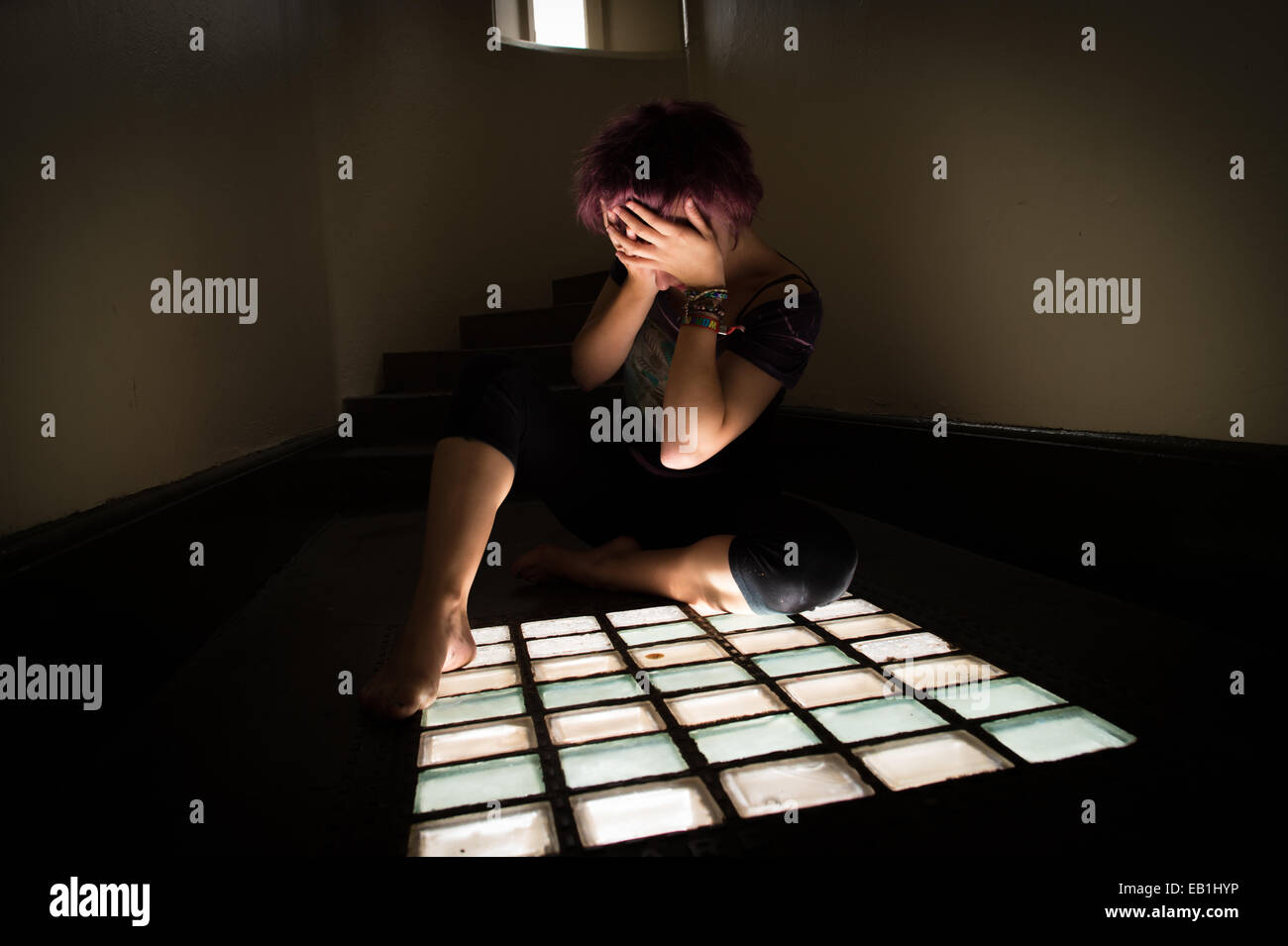 A despairing young teenage girl woman in a prison cell type location with light streaming through a barred window UK Stock Photo