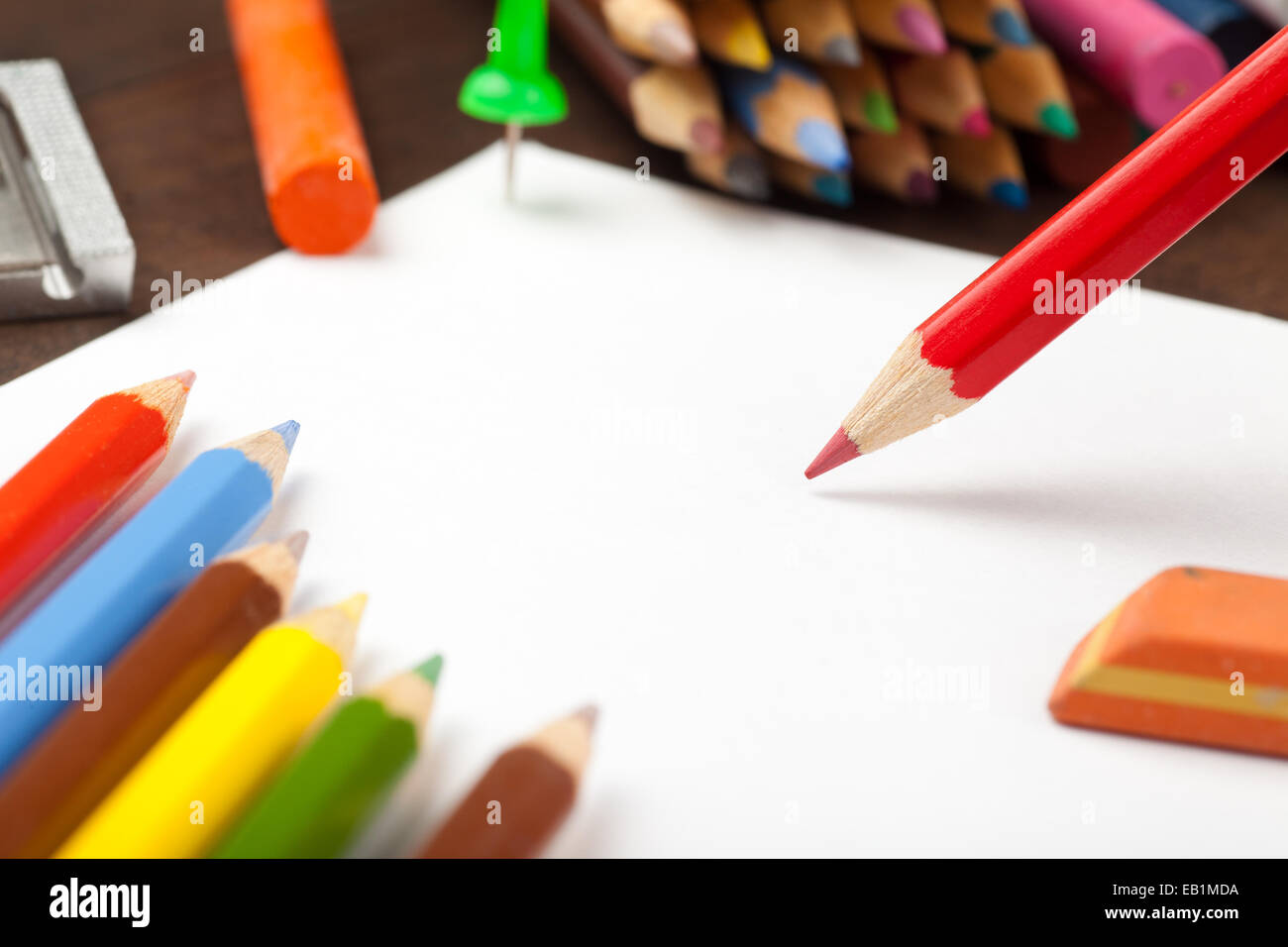 Red pencil draws on white paper sheet. Colored pencils, crayons, eraser