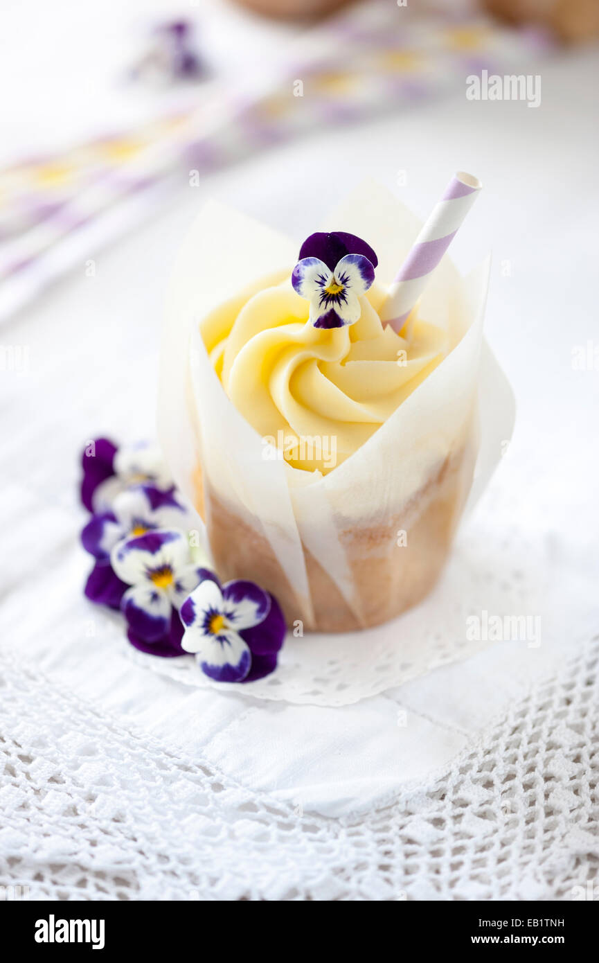 vanilla cupcake with real flower, pansies and decorative straw on vintage white lace tablecloth Stock Photo