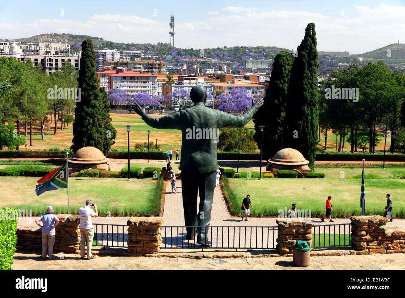 A statue of Nelson Mandela with his arms outstretched with lilac jacaranda blossom in the distance. Stock Photo