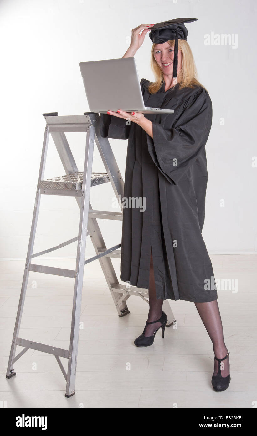 Mature graduate in cap and gown in the workplace using laptop Stock Photo