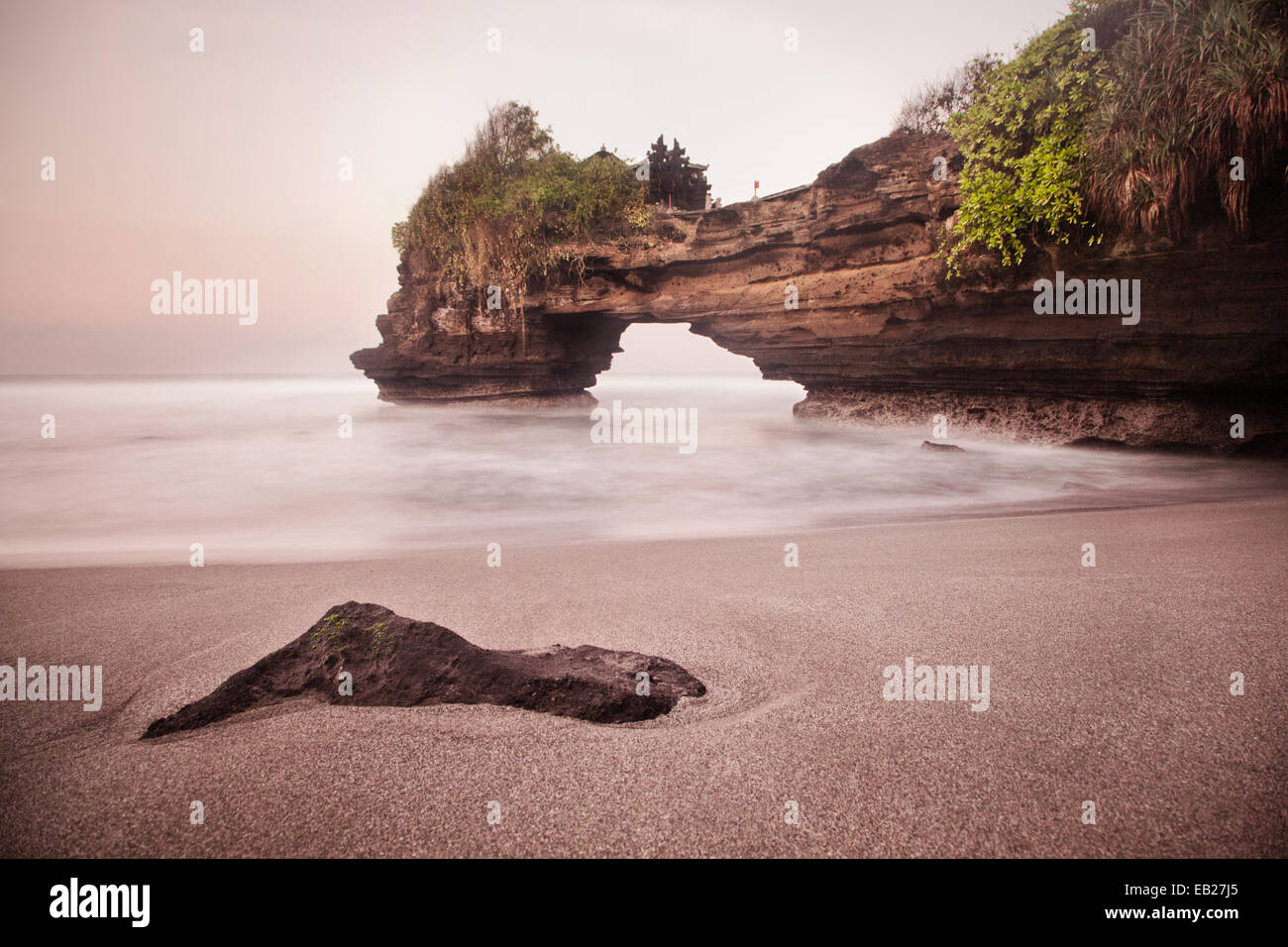Geological phenomenon and natural rock arch with beach and incoming tide at Tanah Lot Temple in Bali. Stunning long exposure seascape image of Karst Stock Photo