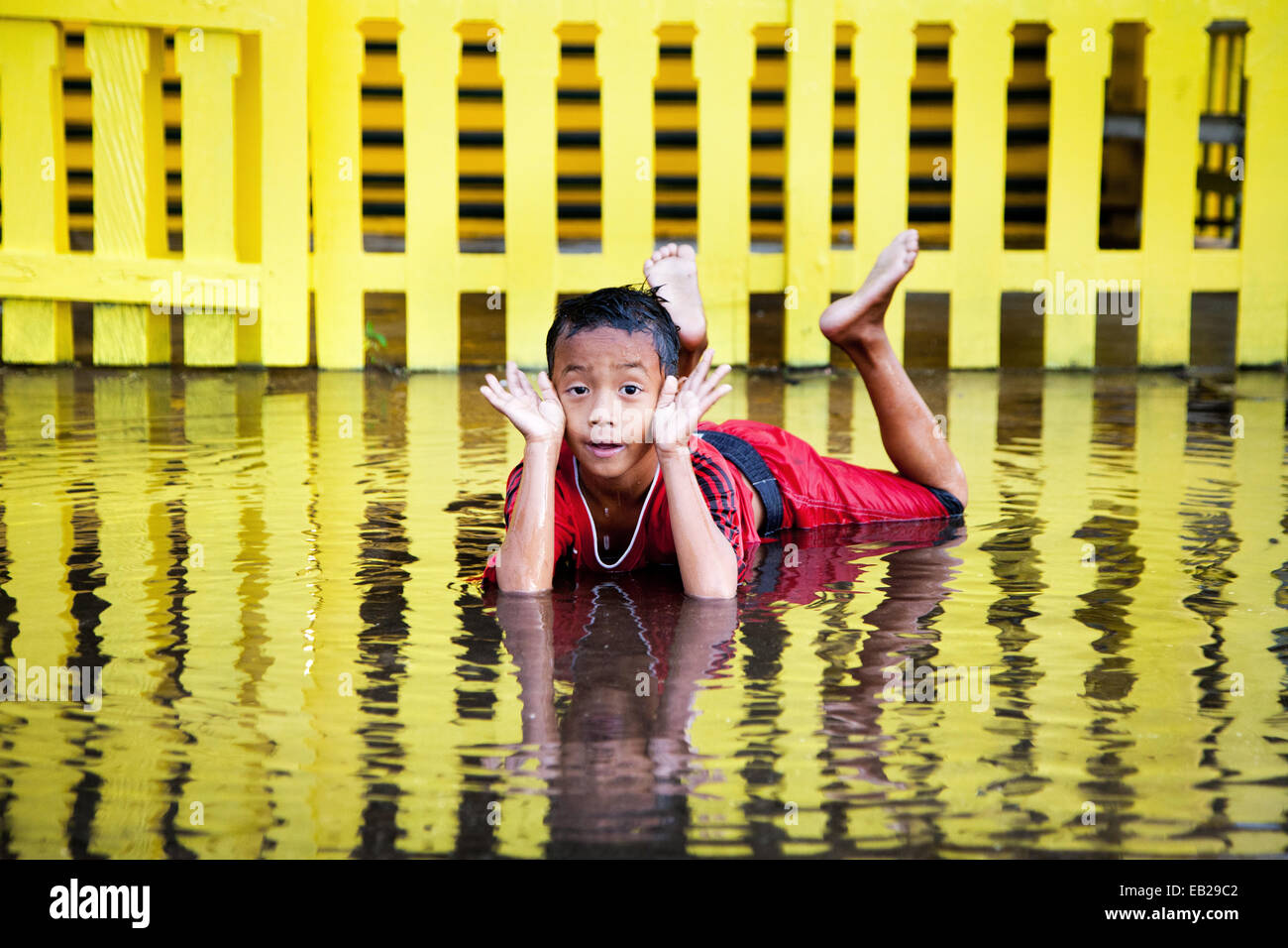 Young Indonesian boy has fun posing and laying in a puddle after heavy tropical rain which is more often than not the norm in Indonesian Borneo! Stock Photo