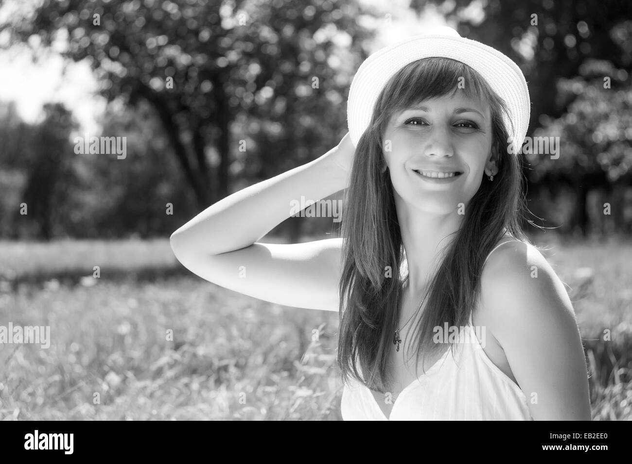 Young cheerful adult girl in summer park. Smiling woman with hat in outdoor environment. Black and white image Stock Photo