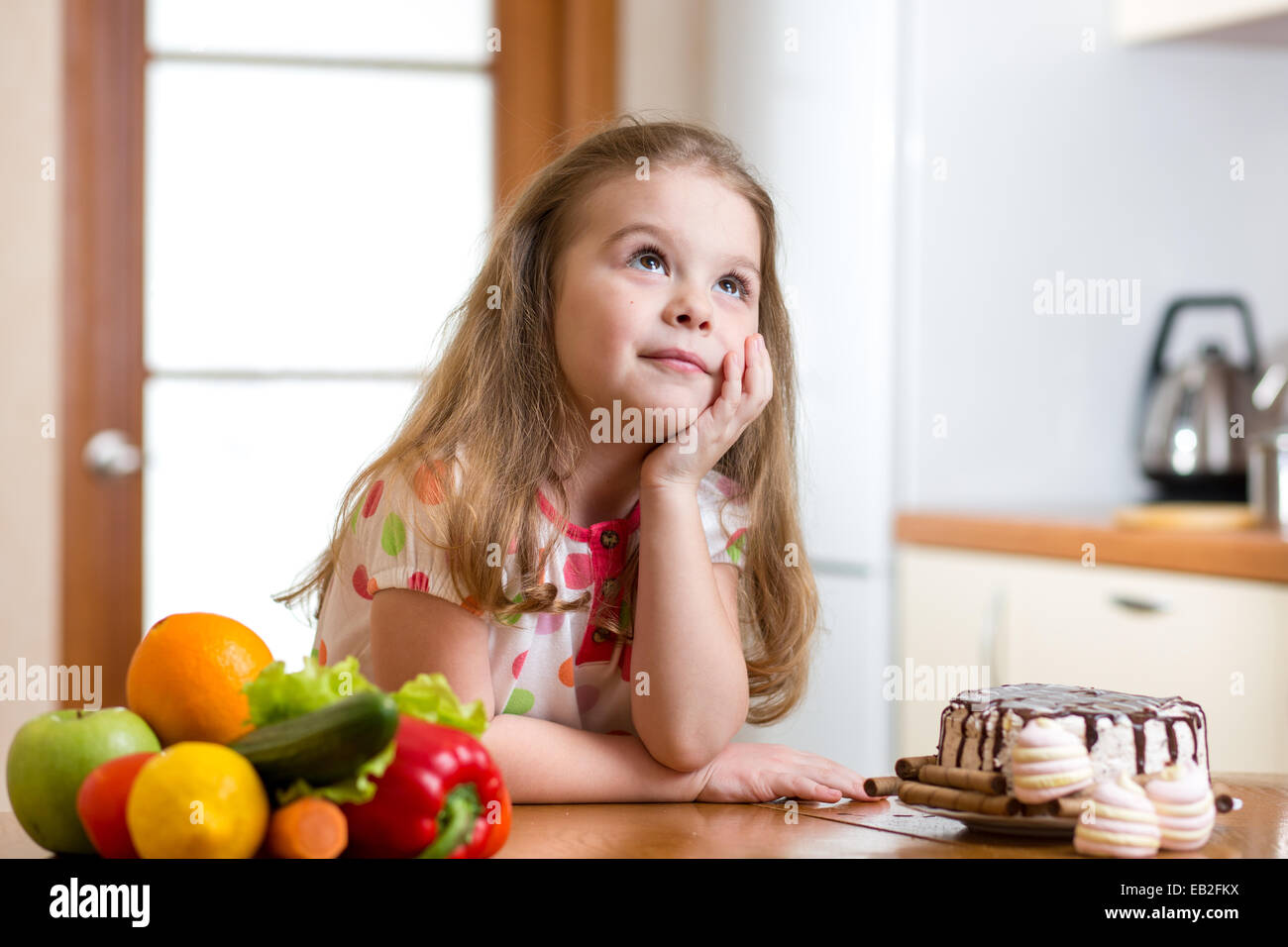 kid choosing between healthy vegetables and tasty sweets Stock Photo