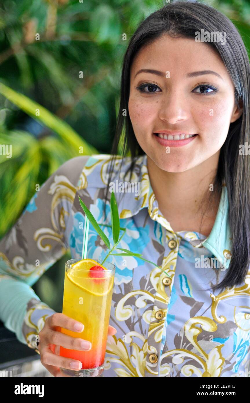 Young Latin American woman drinking a fruit punch by a pool. Stock Photo