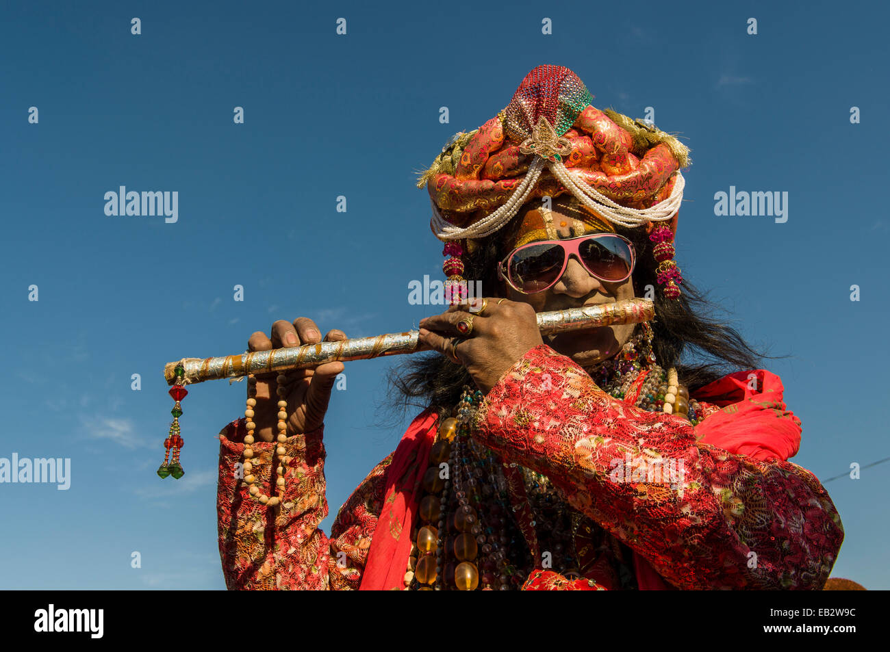 Colourfully costumed devotee playing flute during Kumbh Mela, Allahabad, Uttar Pradesh, India Stock Photo