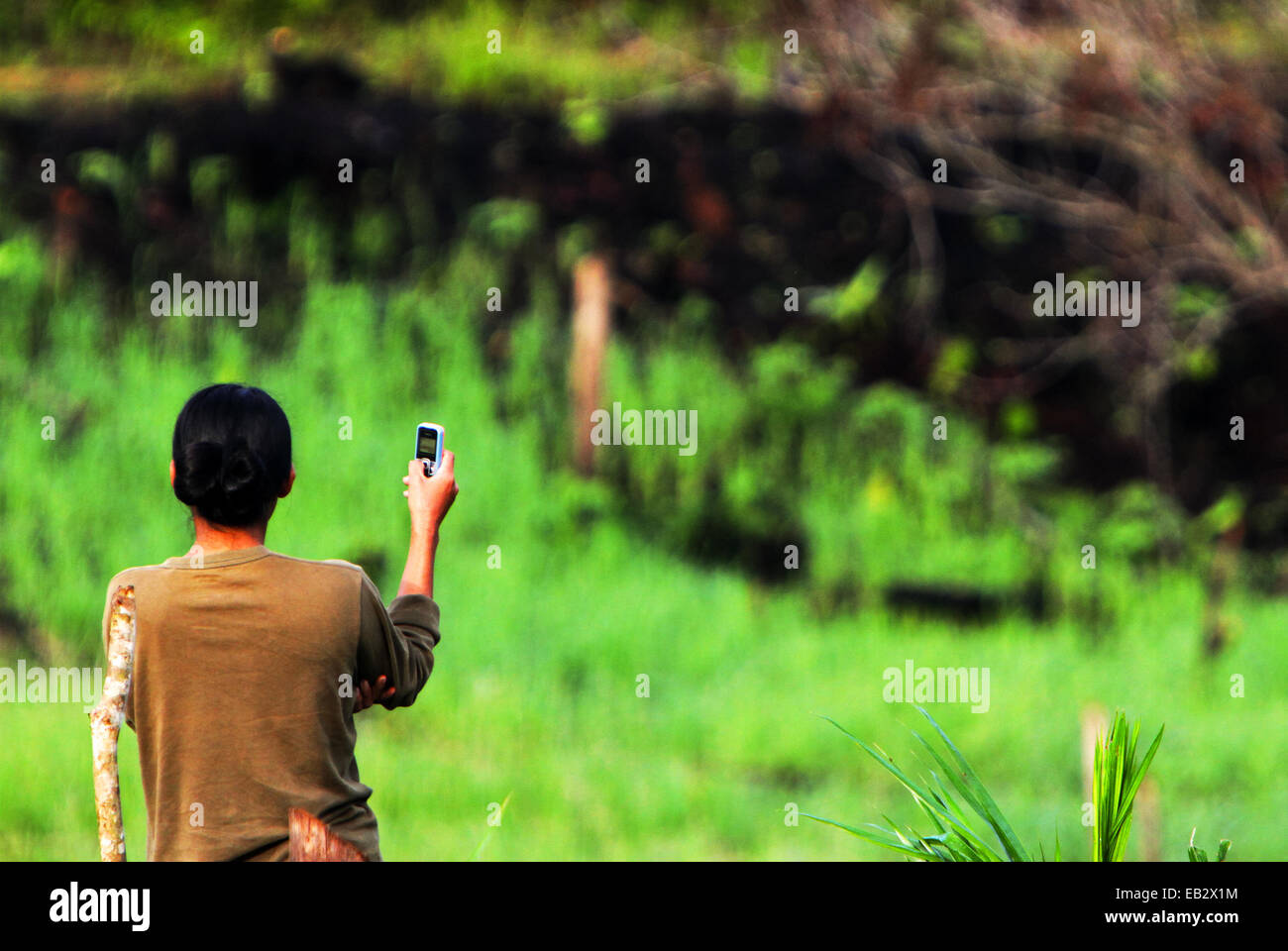 A woman raising her mobile phone in an attempt to capture signal in remote village of Nanga Raun in Kalis, Kapuas Hulu, West Kalimantan, Indonesia. Stock Photo