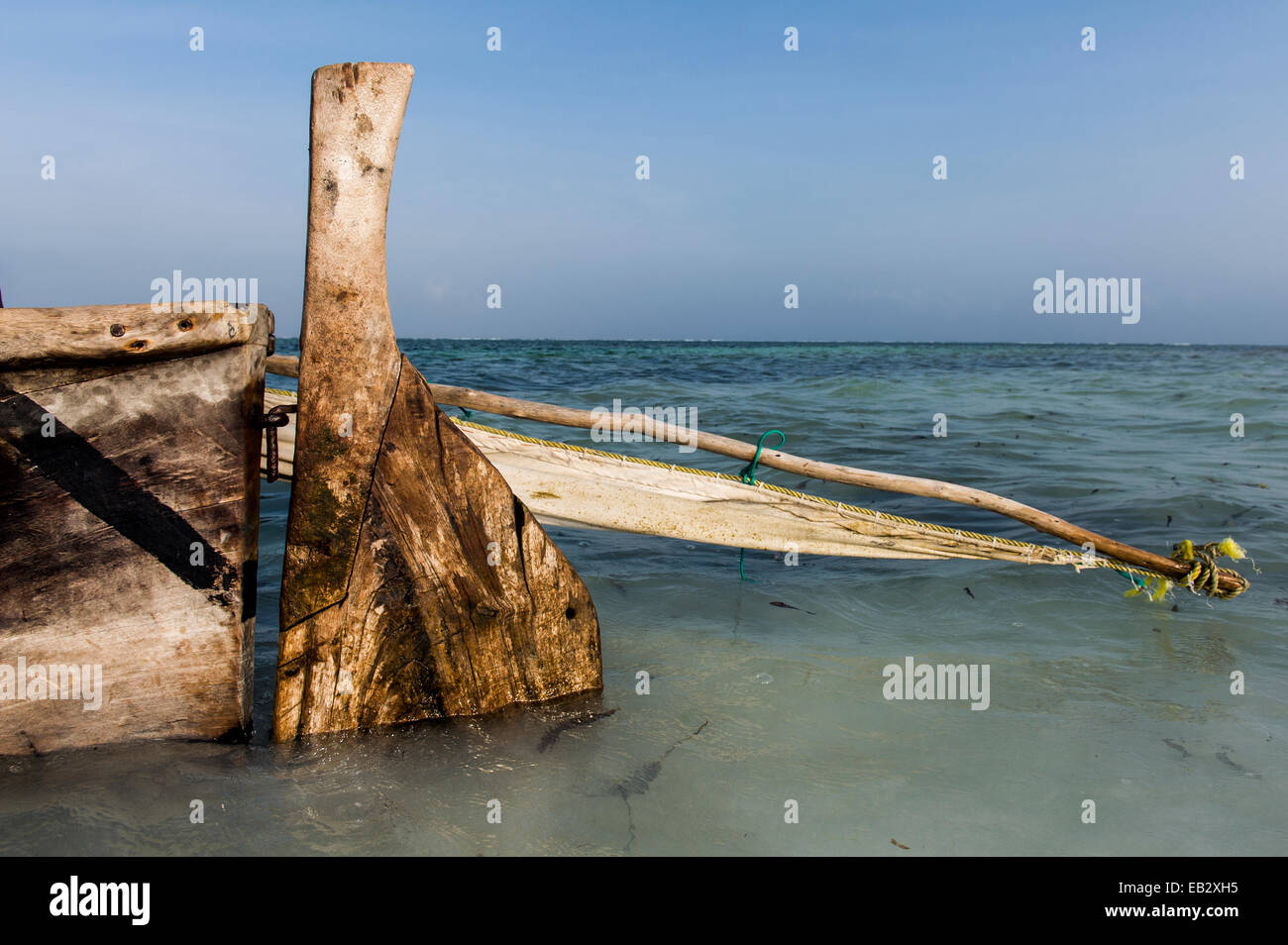 The carved timber rudder, mast and tarpaulin sail of a wooden trimaran fishing dhow moored in the shallows. Stock Photo