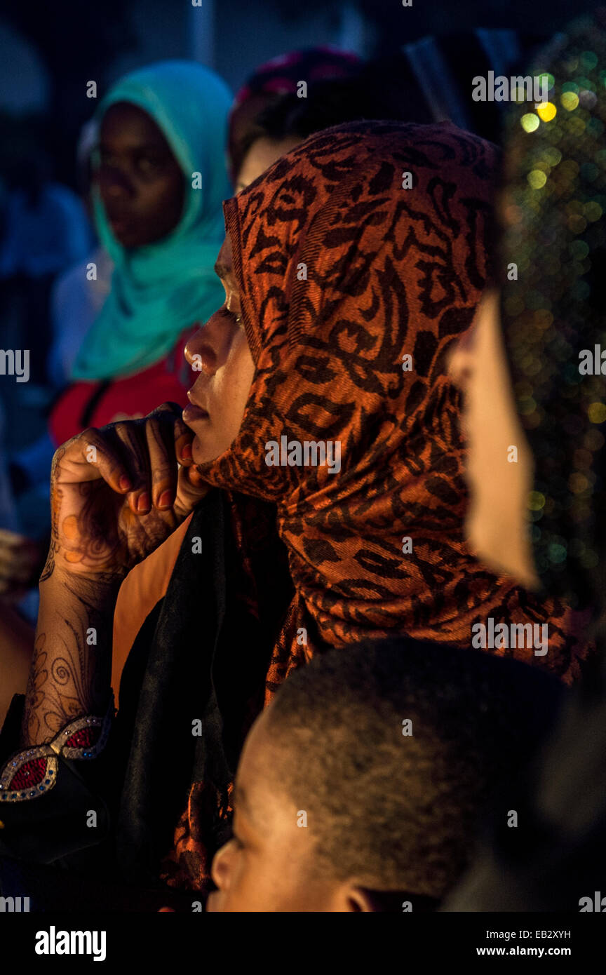 A Muslim woman with henna tattoos waits to be served at a food stall in a crowded night market. Stock Photo