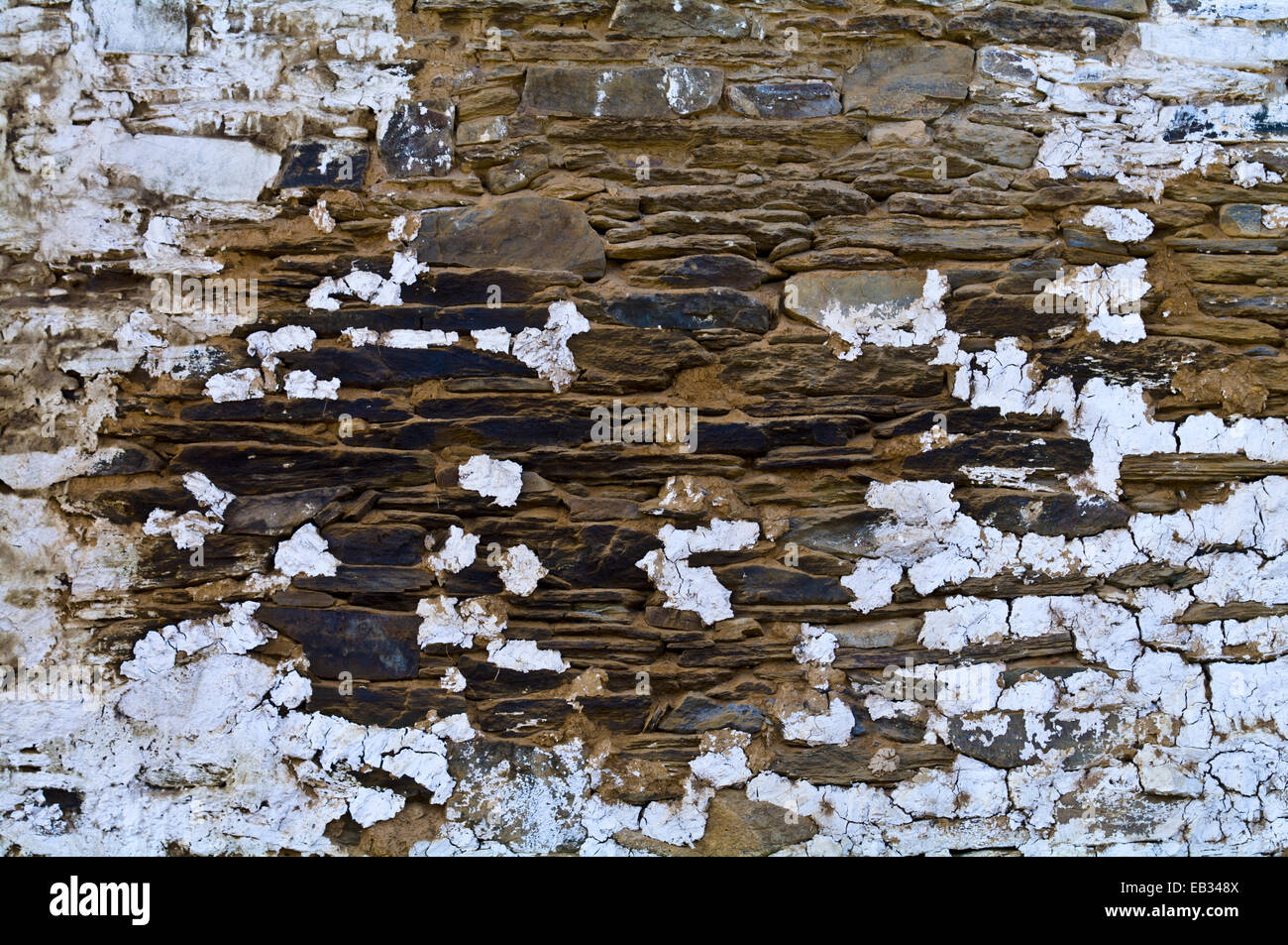 White-wash paint peeling from a weathered handmade stone tiled wall on an ancient Buddhist monastery wall. Stock Photo