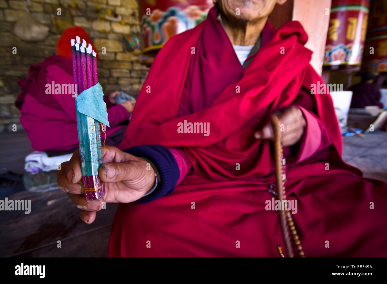 A Buddhist in red robes displays burning dhoop whilst seated beside prayer wheels at the Memorial Chorten. Stock Photo