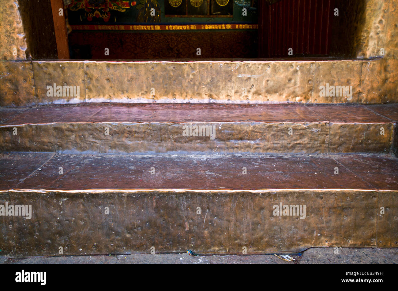 The dinted and worn brass entrance steps of an ancient Buddhist monastery polished by the shuffling feet of monks. Stock Photo