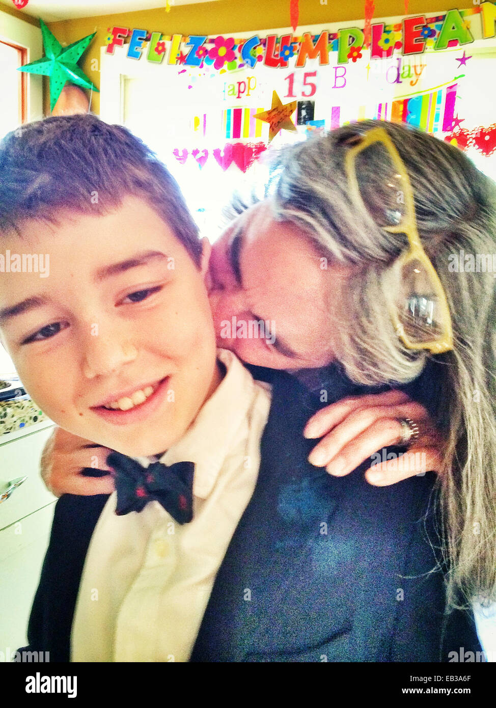 Caucasian mother kissing son in tuxedo at birthday party - Smartphone Captured Stock Image