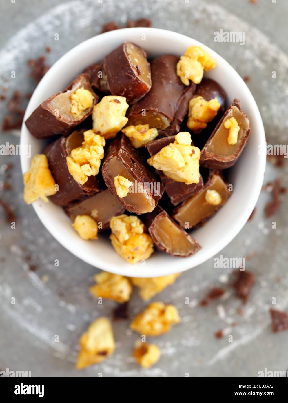 Chocolate candy bars cut into pieces mixed with honeycomb in white porcelain bowl Stock Photo