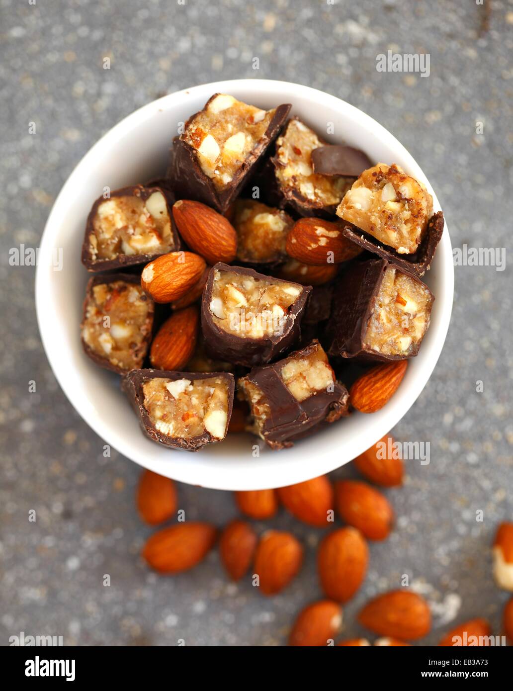 Chocolate candy bars cut into pieces mixed with whole almonds in white porcelain bowl Stock Photo