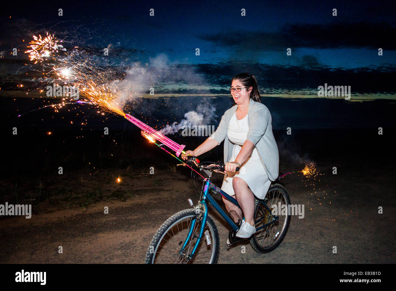 Woman holding fireworks on bicycle at night Stock Photo