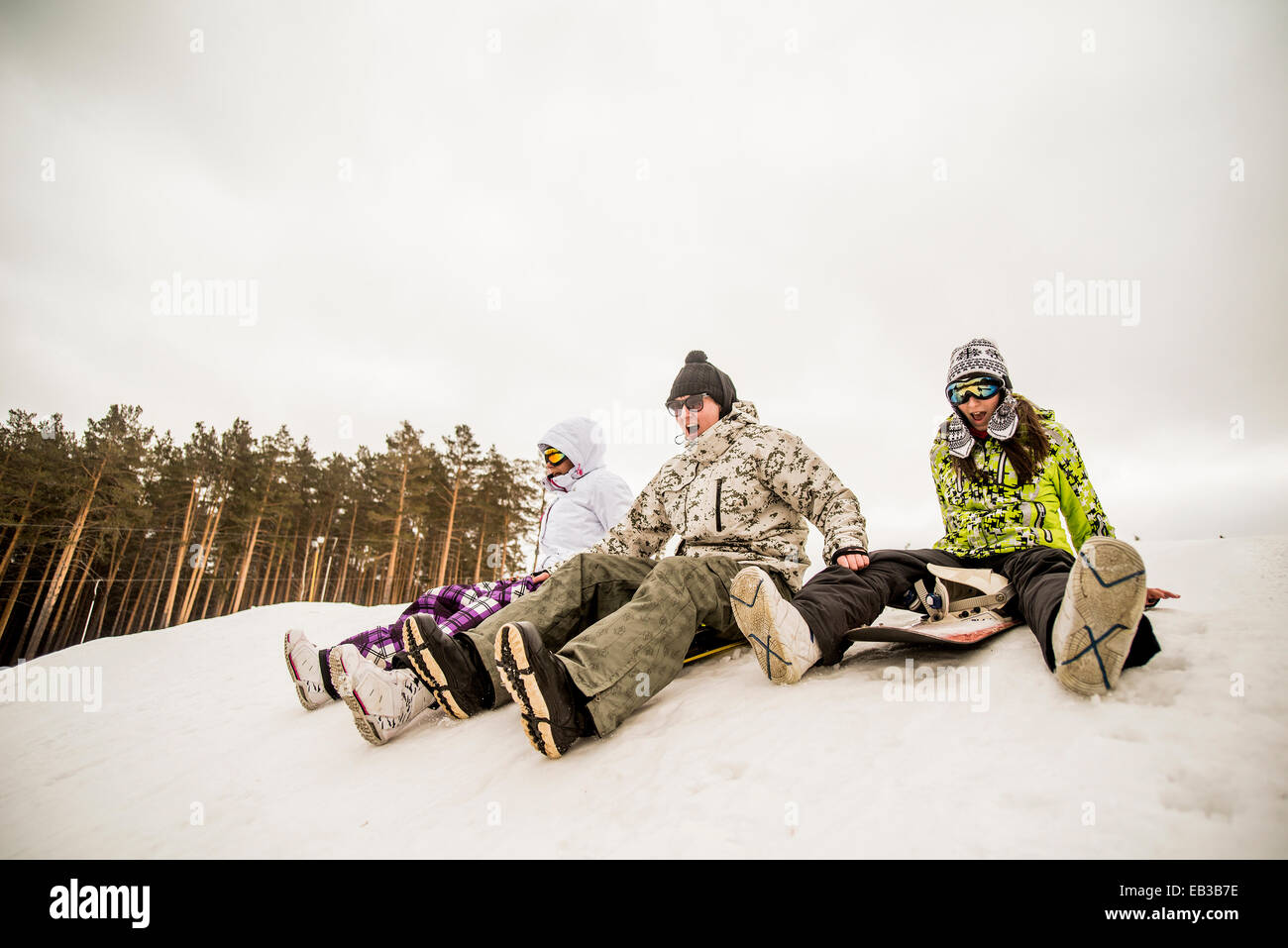 Caucasian friends sitting on snowboards Stock Photo