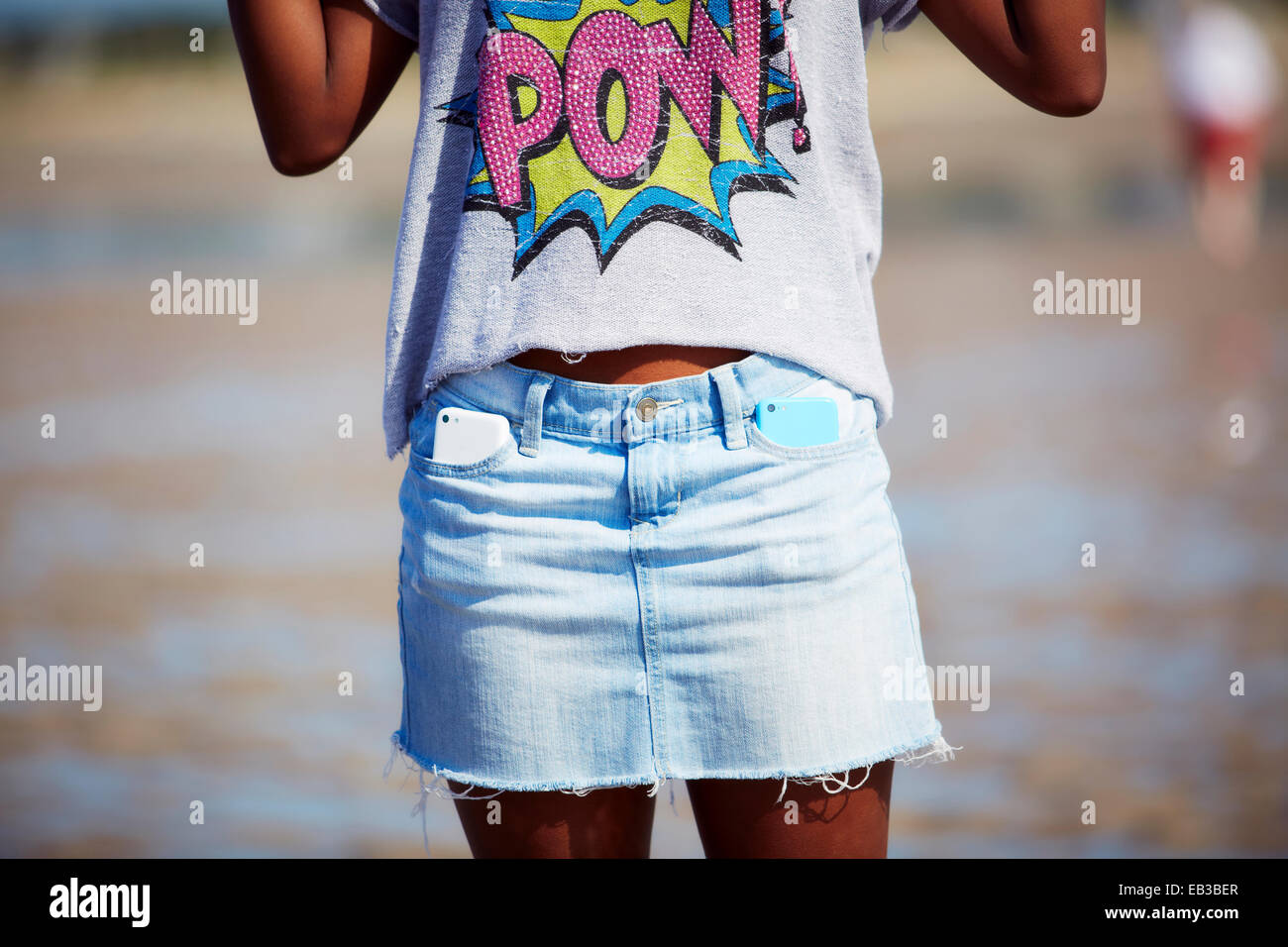 Black teenage girl carrying two cell phones in skirt pockets on beach Stock Photo