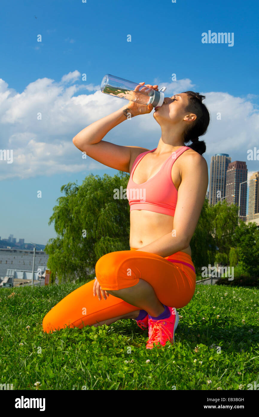 Mixed race woman drinking water in urban park Stock Photo
