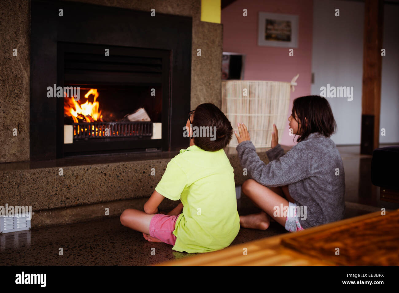 Mixed race children relaxing by fireplace in living room Stock Photo