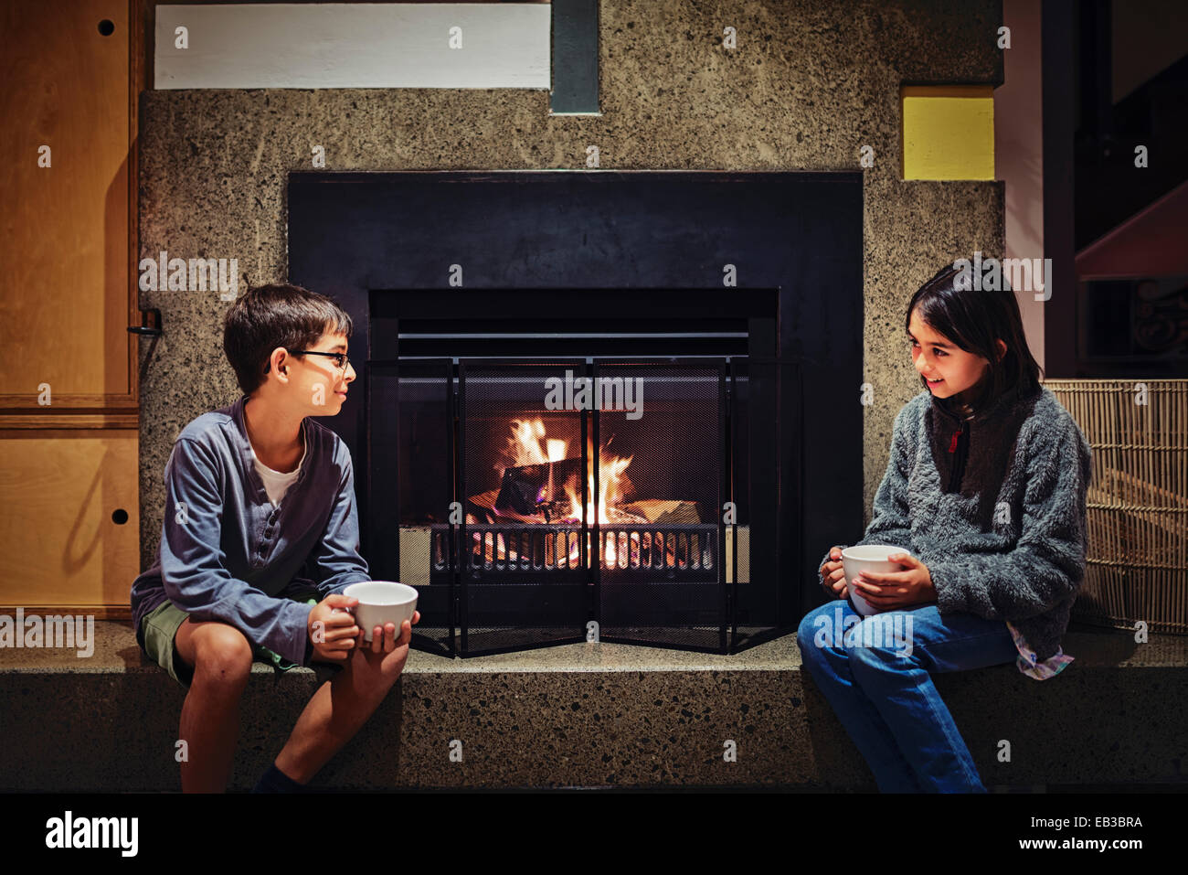 Mixed race children having hot drink together near fireplace Stock Photo
