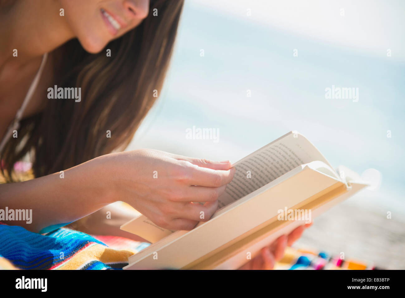 Caucasian woman reading book on beach Stock Photo