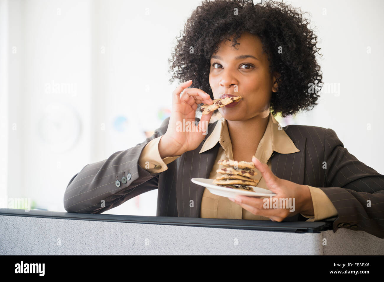 Businesswoman eating stack of cookies in cubicle Stock Photo