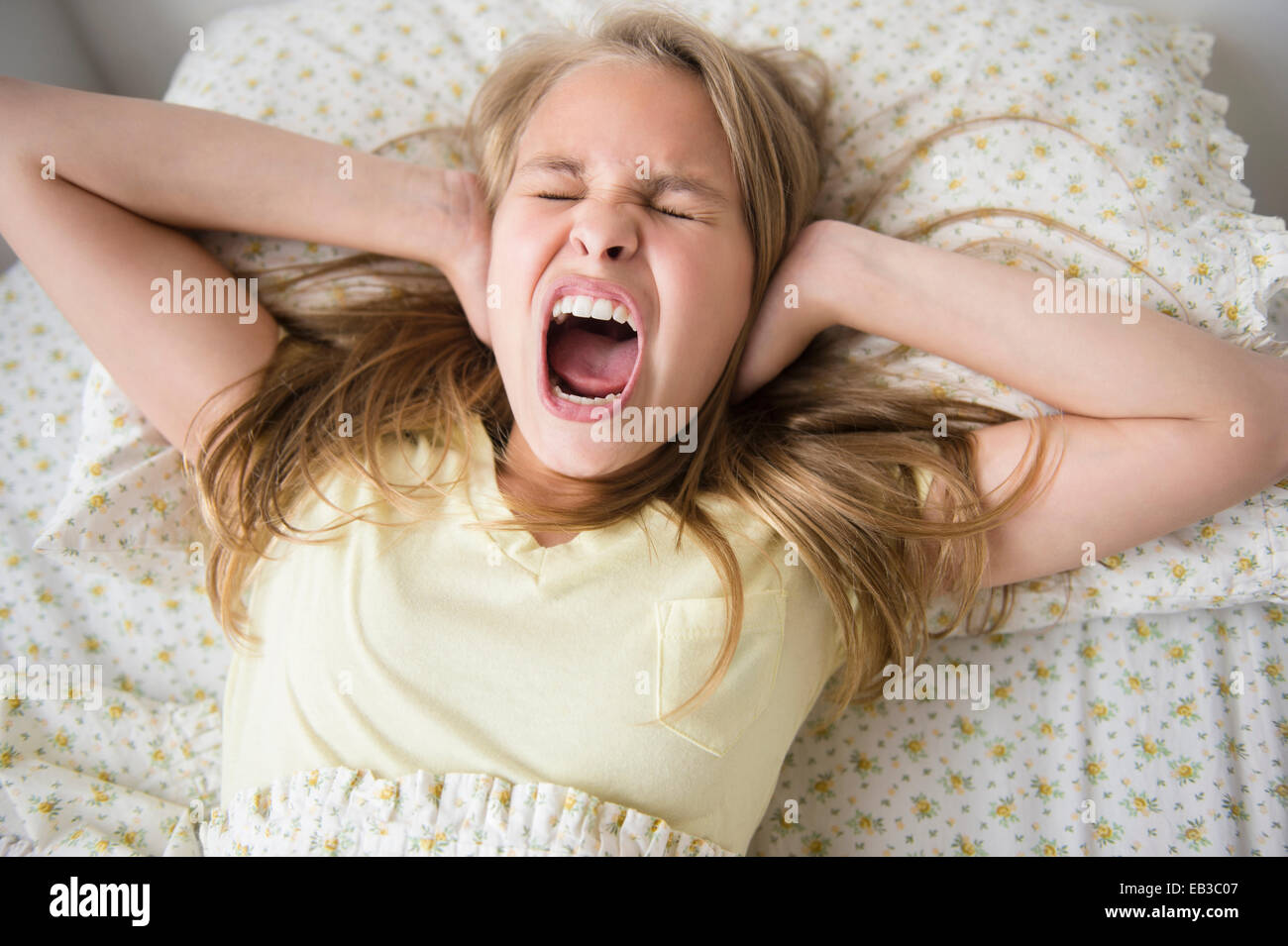 Shouting Caucasian girl covering her ears on bed Stock Photo